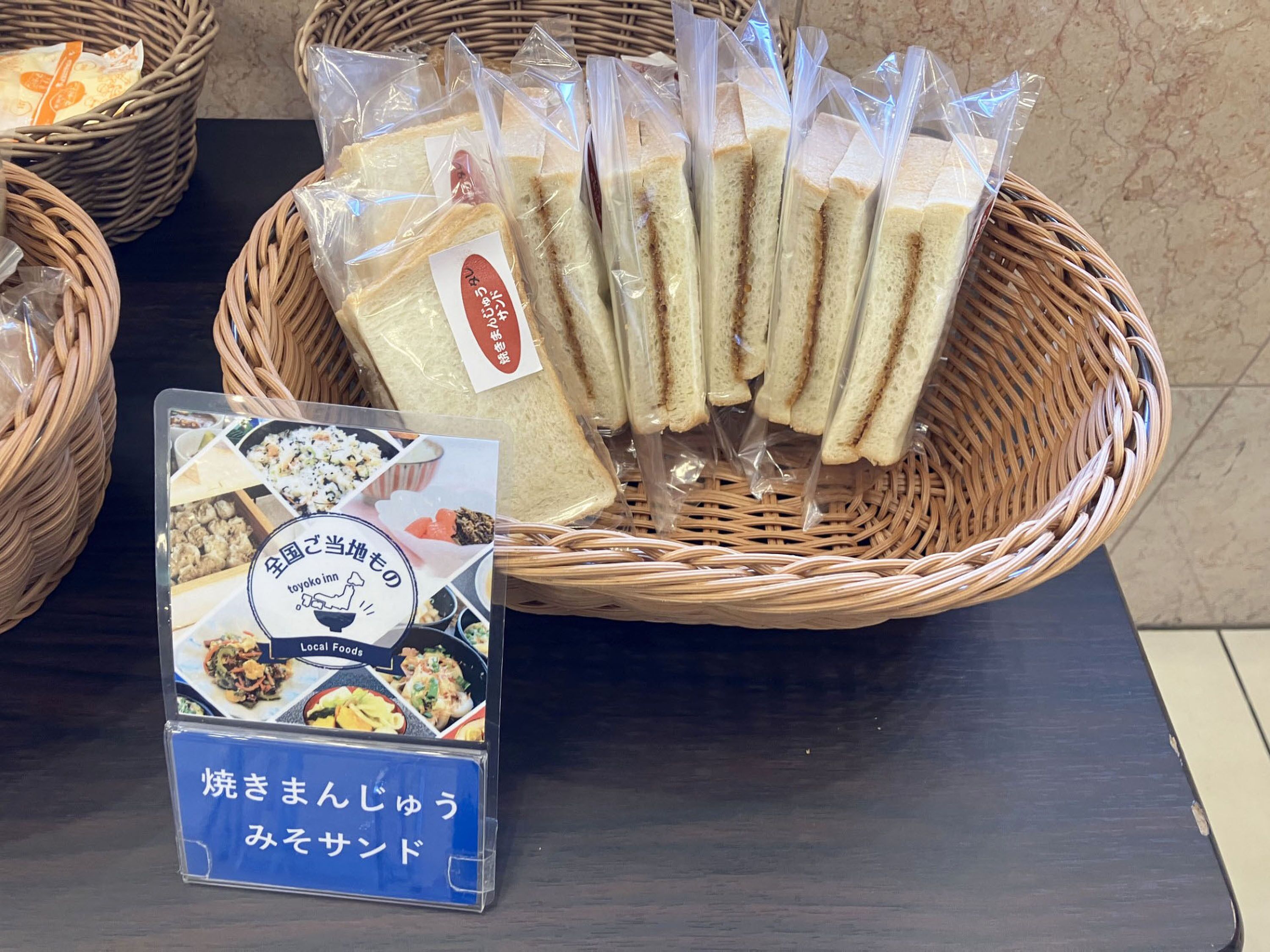 A display of packaged sandwiches and a signboard with food images and Japanese text.