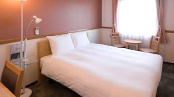 A hotel room with a large bed, a desk with a lamp, a chair, a small table, and a window with curtains.