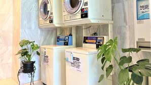 A laundry area with two washing machines and a dryer, a potted plant, and a sign with instructions.