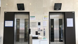 Two elevators with glass doors, a small white counter with a bottle, and informational signs on the wall. - Toyoko Inn Kenkyu-gakuen Ekimae (Tsukuba)