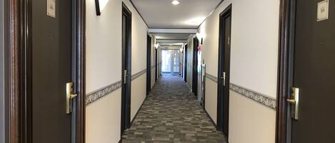Un pasillo largo y estrecho con pisos alfombrados y puertas a ambos lados, que conduce a habitaciones.