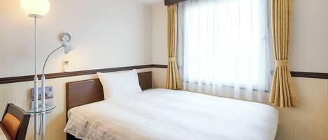 A hotel room with a neatly made bed, a bedside lamp, a clock on the wall, and a window with curtains.