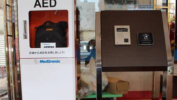 Een Medtronic AED apparaat in een witte doos met een rood label, geplaatst naast een bruine kast met een bedieningspaneel.