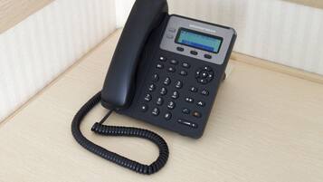 A black telephone with a keypad and a small screen, placed on a wooden surface.
