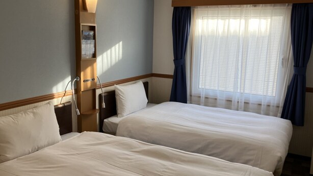 Une chambre d’hôtel avec deux lits, une table de chevet, une lampe et une fenêtre avec des rideaux.