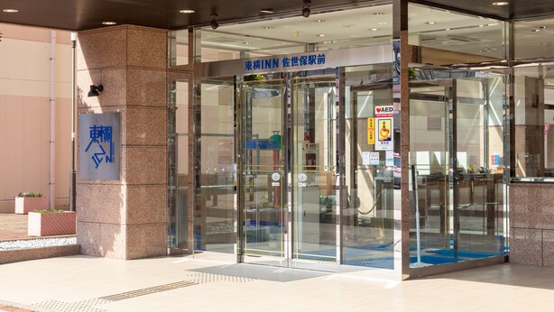 A modern building entrance with glass doors, a sign indicating an emergency exit, and a wheelchair-accessible ramp. - Toyoko Inn Sasebo Ekimae (Sasebo)
