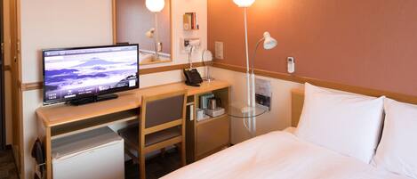 A hotel room with a bed, a desk with a computer, a telephone, a mirror, and a wall clock.