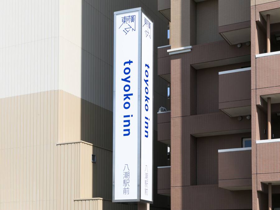 Une enseigne verticale pour l’hôtel Toyoko Inn, avec du texte en japonais, fixée sur un bâtiment.