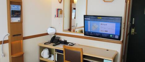 A hotel room with a desk, chair, bed, bedside table, mirror, clock, and a television displaying a message in Japanese.