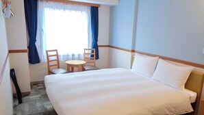 A hotel room with a large bed, a small round table with two chairs, a window with blue curtains, and a carpeted floor. - Toyoko Inn Tokushima Ekimae (Tokushima)