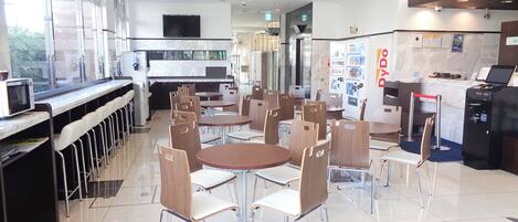 Een moderne cafetaria met ronde tafels en stoelen, een keukenhoek en een automaat.