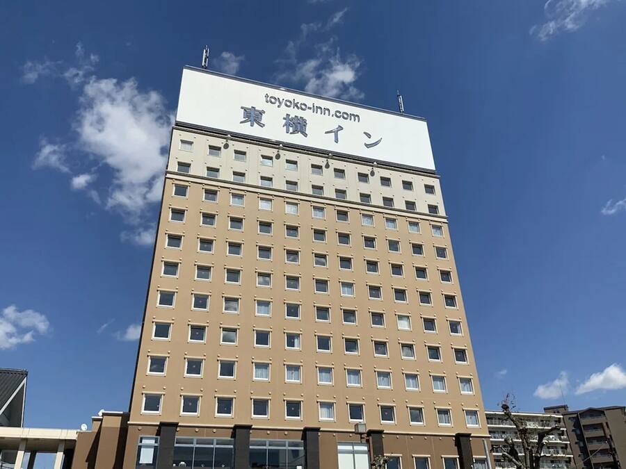 Un edificio de hotel alto con un letrero que dice 'toyoko-inn.com' y caracteres japoneses.