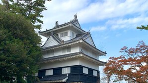 Ett traditionellt japanskt slott med en vit och svart fasad, en grund av sten och ett markant tak täckt med tegelpannor.