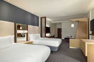 Quarto de hotel com duas camas, uma escrivaninha, uma cadeira, televisão e minibar.