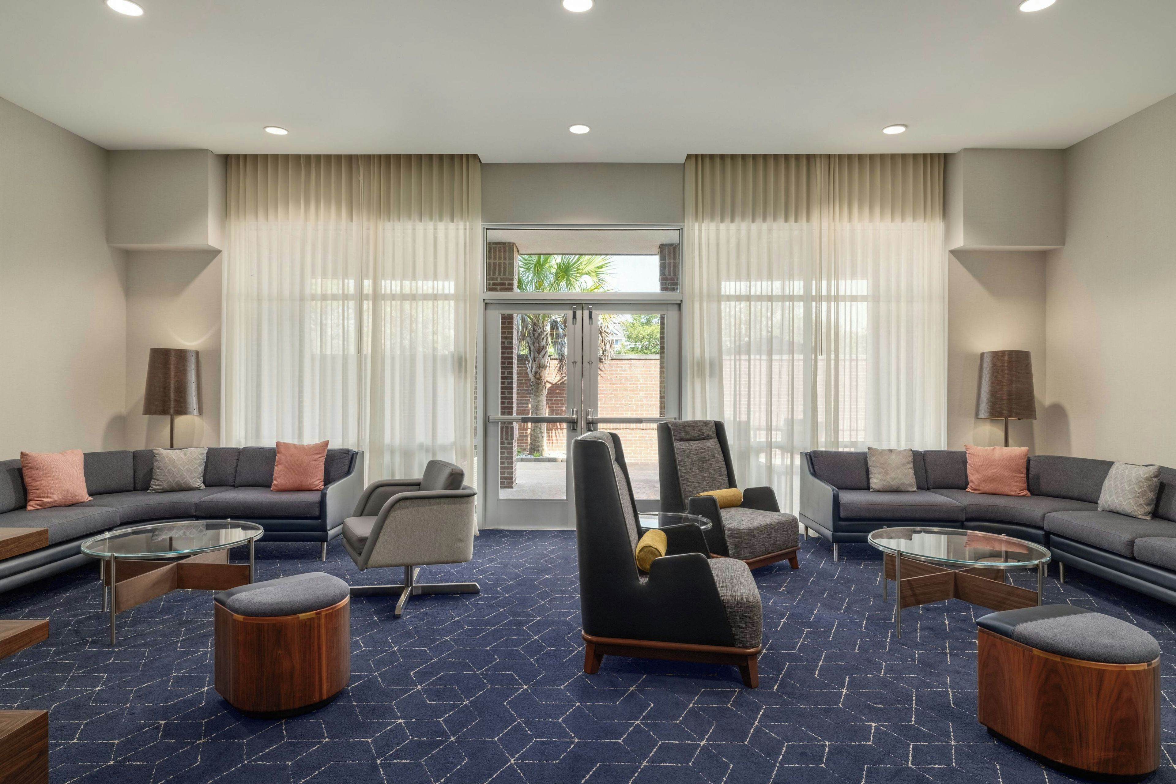 Un moderno vestíbulo de hotel con zona de estar, una mesa de centro y un amplio ventanal con cortinas.