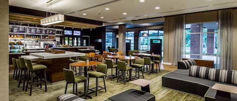 A modern hotel lobby with a bar area, seating arrangements, and large windows offering a view of the outdoors.