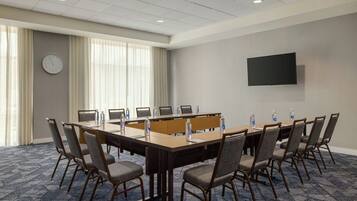 A conference room with a long table, chairs, a clock, and a TV on the wall.