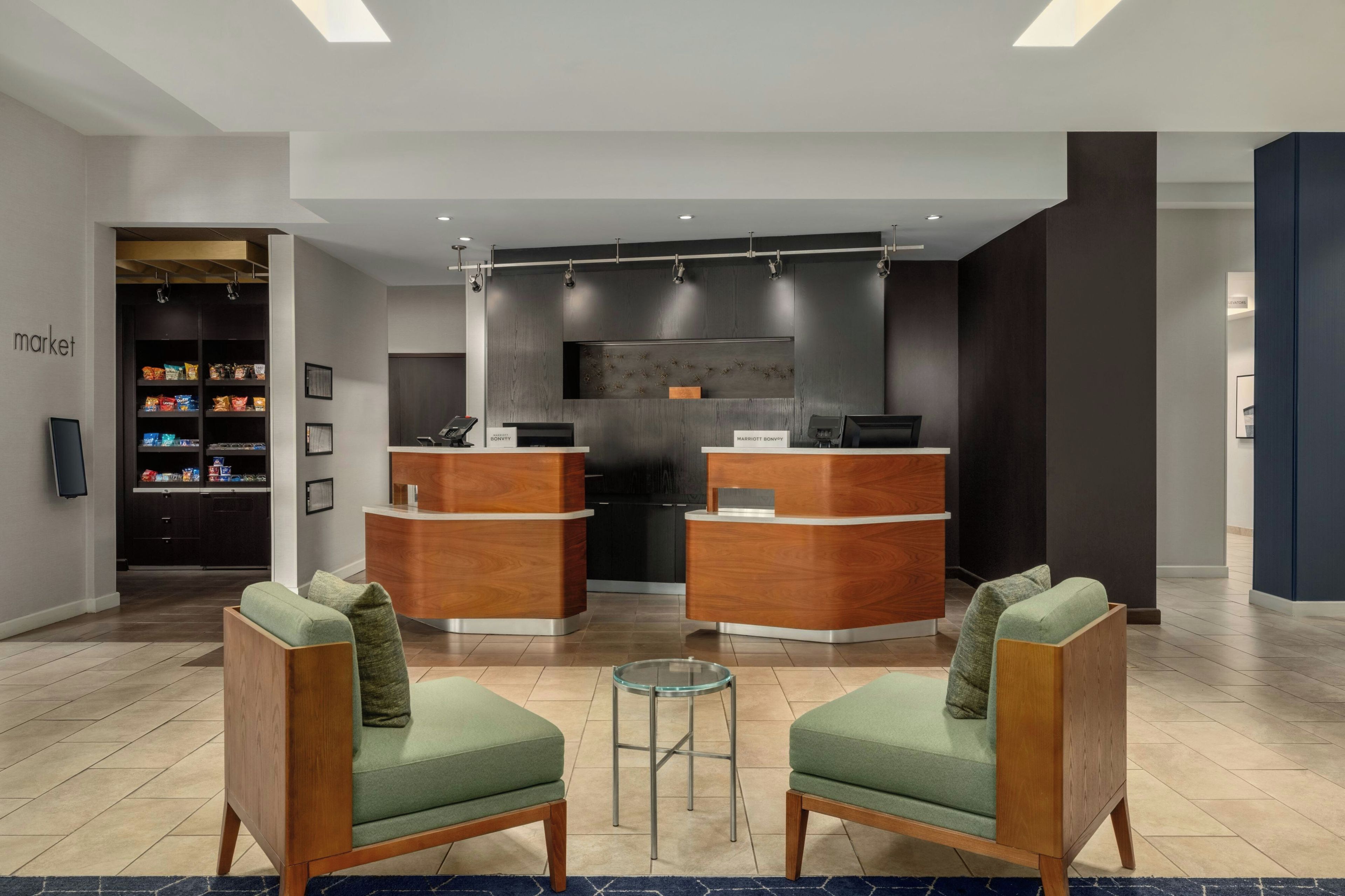A hotel lobby with two reception desks, a seating area with two chairs, and a snack bar.