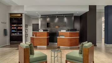 A hotel lobby with two reception desks, a seating area with two chairs, and a snack bar.