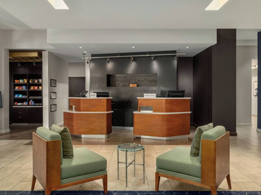 A hotel lobby with two reception desks, a seating area with two chairs, and a snack bar.