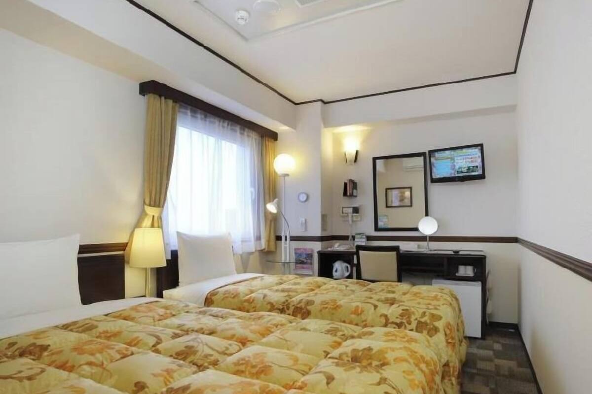 A hotel room with two beds, a desk, a chair, a TV, and a window with curtains.