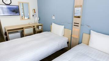 A hotel room with two single beds, a desk with a chair, a small refrigerator, a clock, and a mirror.