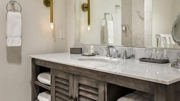 Une salle de bain dotée d’un grand miroir, de deux lavabos et d’un meuble-lavabo avec des étagères pour les serviettes.