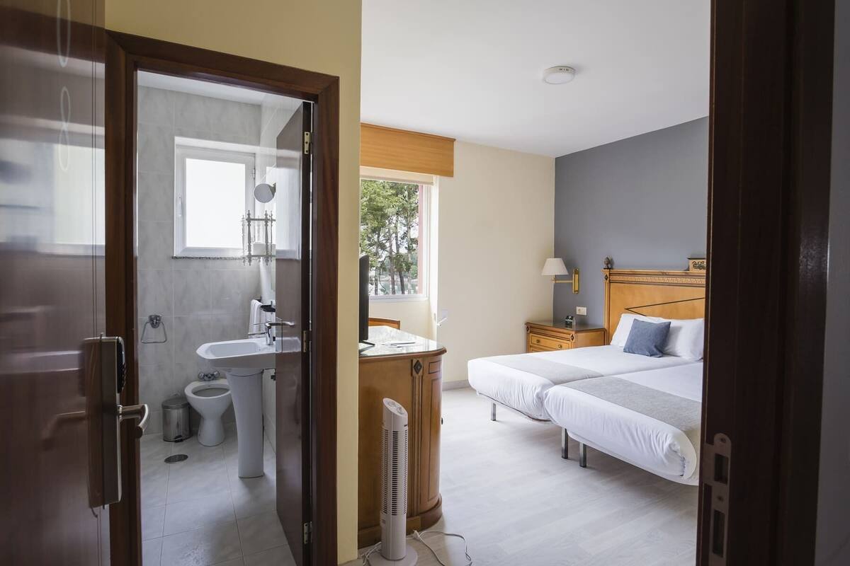 A hotel room with a bed, bedside table, lamp, and a view of the outdoors.