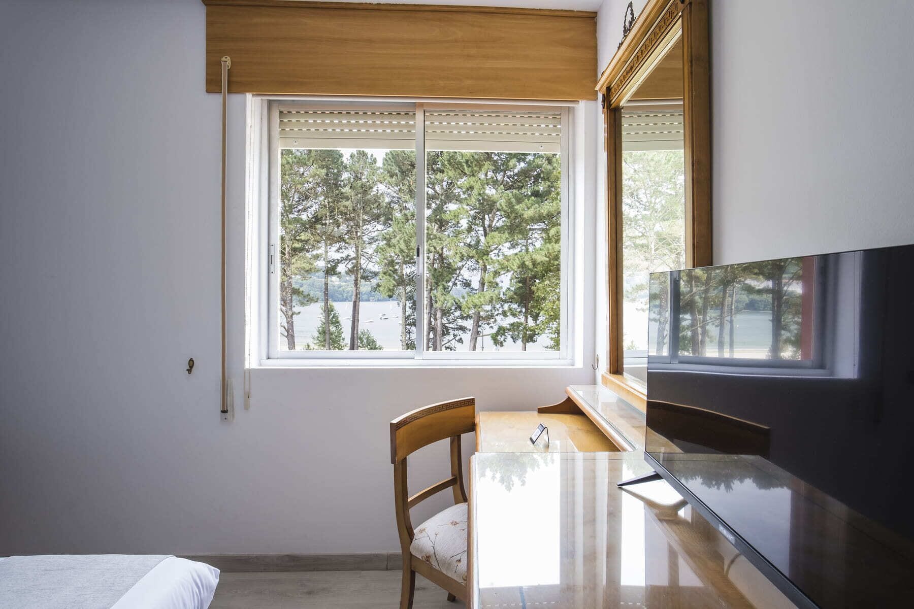 Una habitación con un ventanal grande, una silla de madera, una mesa y un televisor de pantalla plana.