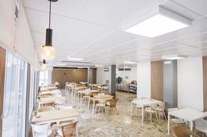 Un comedor amplio con varias mesas y sillas, una zona de cocina y un diseño de techo moderno.