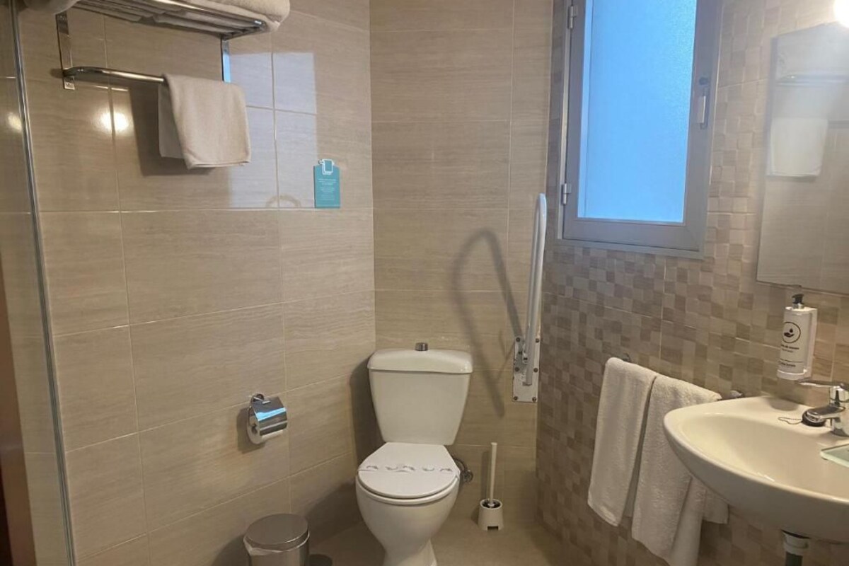 A bathroom with a toilet, bidet, sink, and a window.
