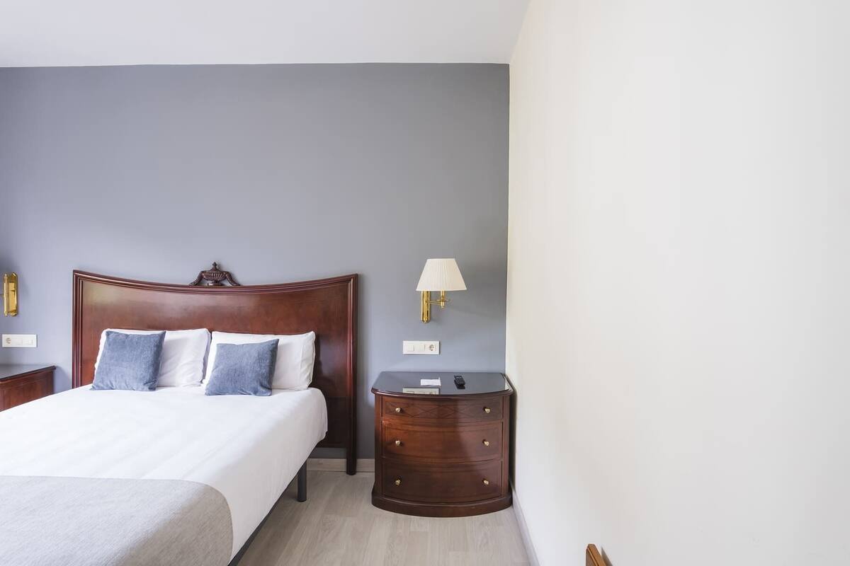 A neatly arranged hotel room with a large bed, a bedside table with a lamp, and a dresser.