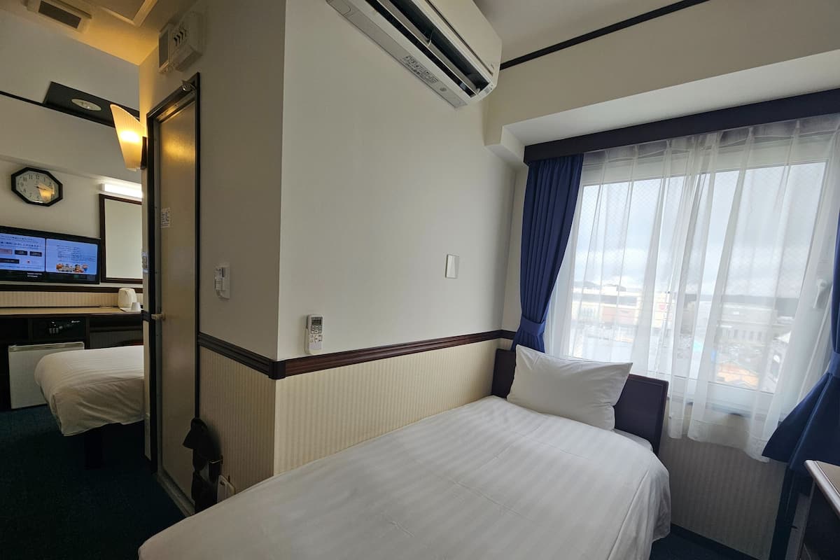 Hotelkamer met twee bedden, een bureau met een computer, een klok en een airconditioning.
