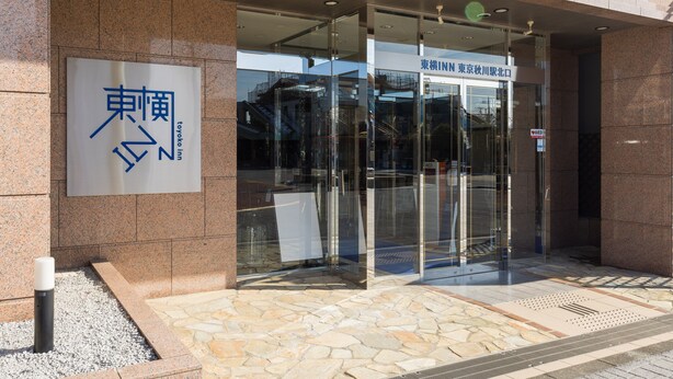 La entrada a un edificio con un letrero que dice "TOYOKO INN" y una puerta de vidrio con un letrero que indica "AED" para asistencia de emergencia.