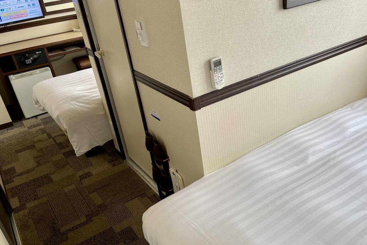 A hotel room with two beds, a desk with a computer, and a wall-mounted TV.