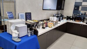 Montaje de bufé con diversos alimentos y utensilios, un reloj en la pared y un mantel azul.