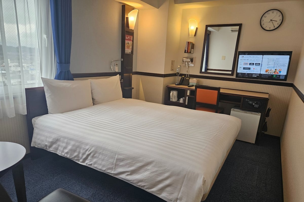 Een hotelkamer met een groot bed, een bureau met een computer, een klein tafeltje en een stoel.