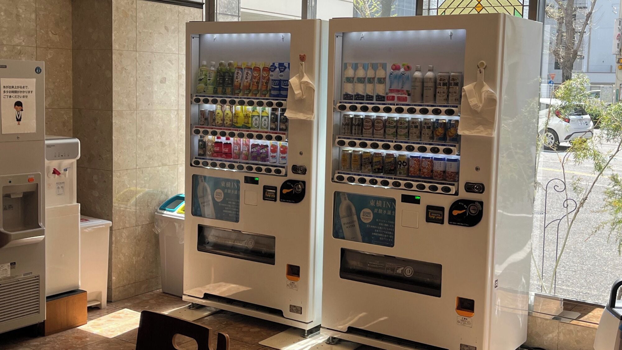 Dos máquinas expendedoras de bebidas con una variedad de opciones y un dispensador de agua a la izquierda.