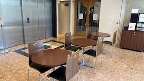 Una hall con una macchina del caffè, un ascensore chiuso e un'area salotto con tavoli e sedie.