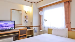 Una camera d'albergo con letto, scrivania, sedia, televisore, telefono, lampada e finestra con tende.