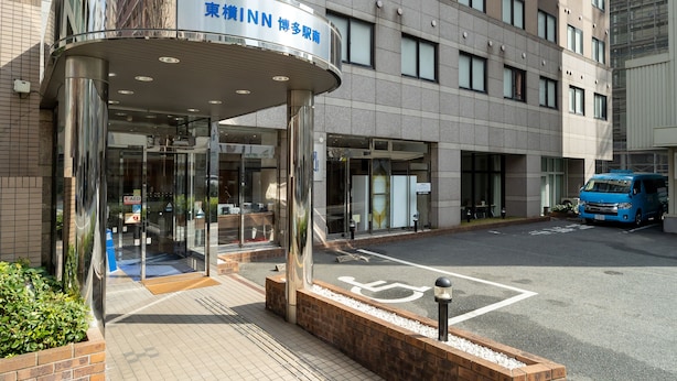 L'ingresso moderno di un hotel con una tettoia in vetro, un furgone blu parcheggiato fuori e una chiara vista sulla facciata dell'edificio.