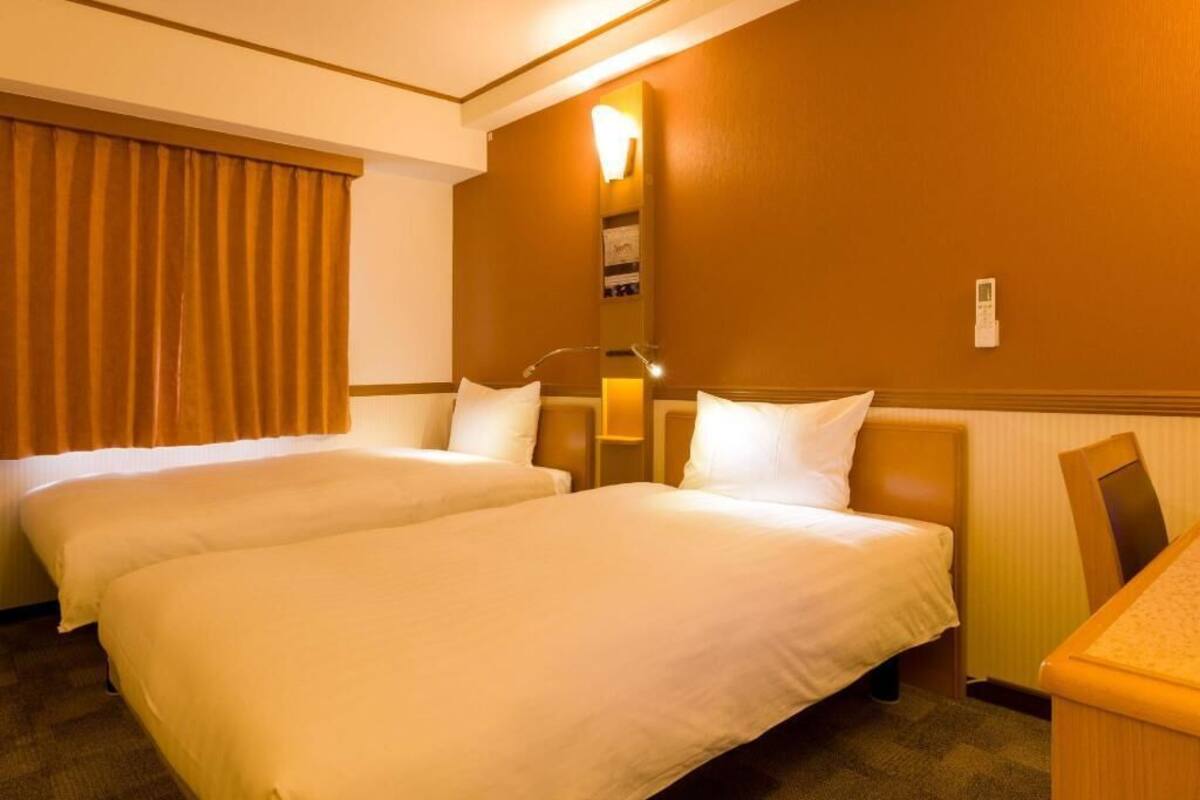 Habitación de hotel con dos camas, una mesita de noche, una lámpara y un teléfono en la pared.