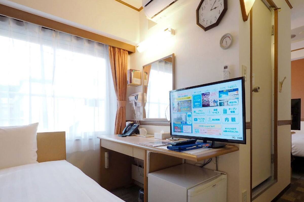 Habitación de hotel con cama, escritorio, computadora y un reloj en la pared.