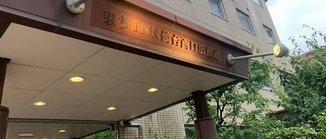 The entrance of a building with a sign in a foreign language, a covered walkway, and a street lamp.