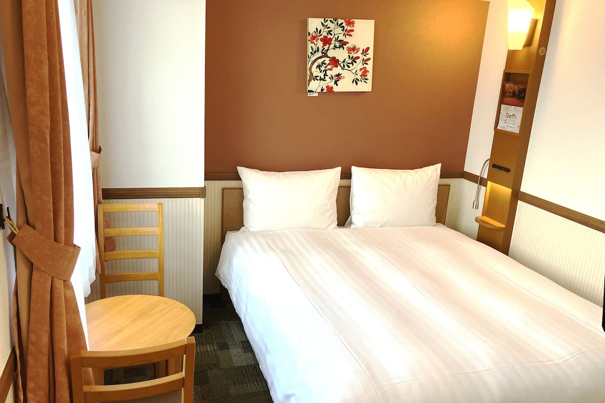 Une chambre d’hôtel avec un lit, une chaise en bois, une table et un tableau accroché au mur.