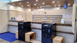 Een receptiezone met een balie, twee zwarte self-service kiosken, een klok en een beveiligingscamera.