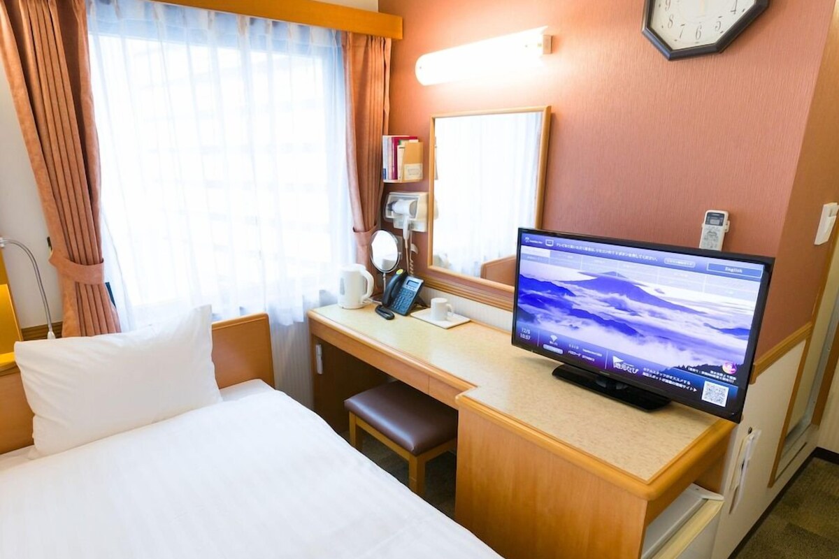 A hotel room with a bed, desk, and a flat-screen TV displaying a scenic wallpaper.