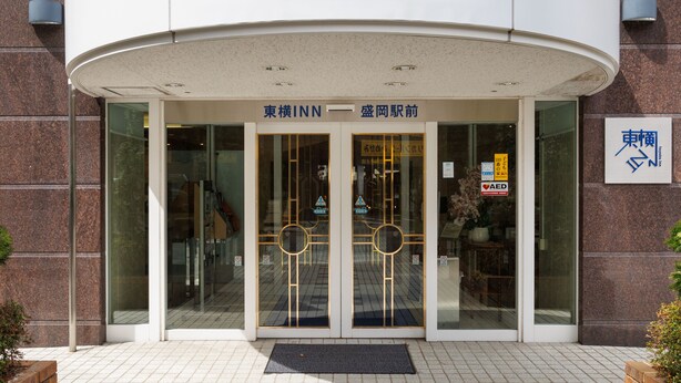 Een hotel ingang met een gebogen dak, glazen deuren met een gouden lijst, en borden in zowel Engels als Japans.
