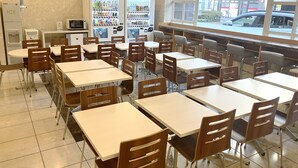 Een cafetaria met tafels, stoelen, automaten en een raam met uitzicht op de straat.