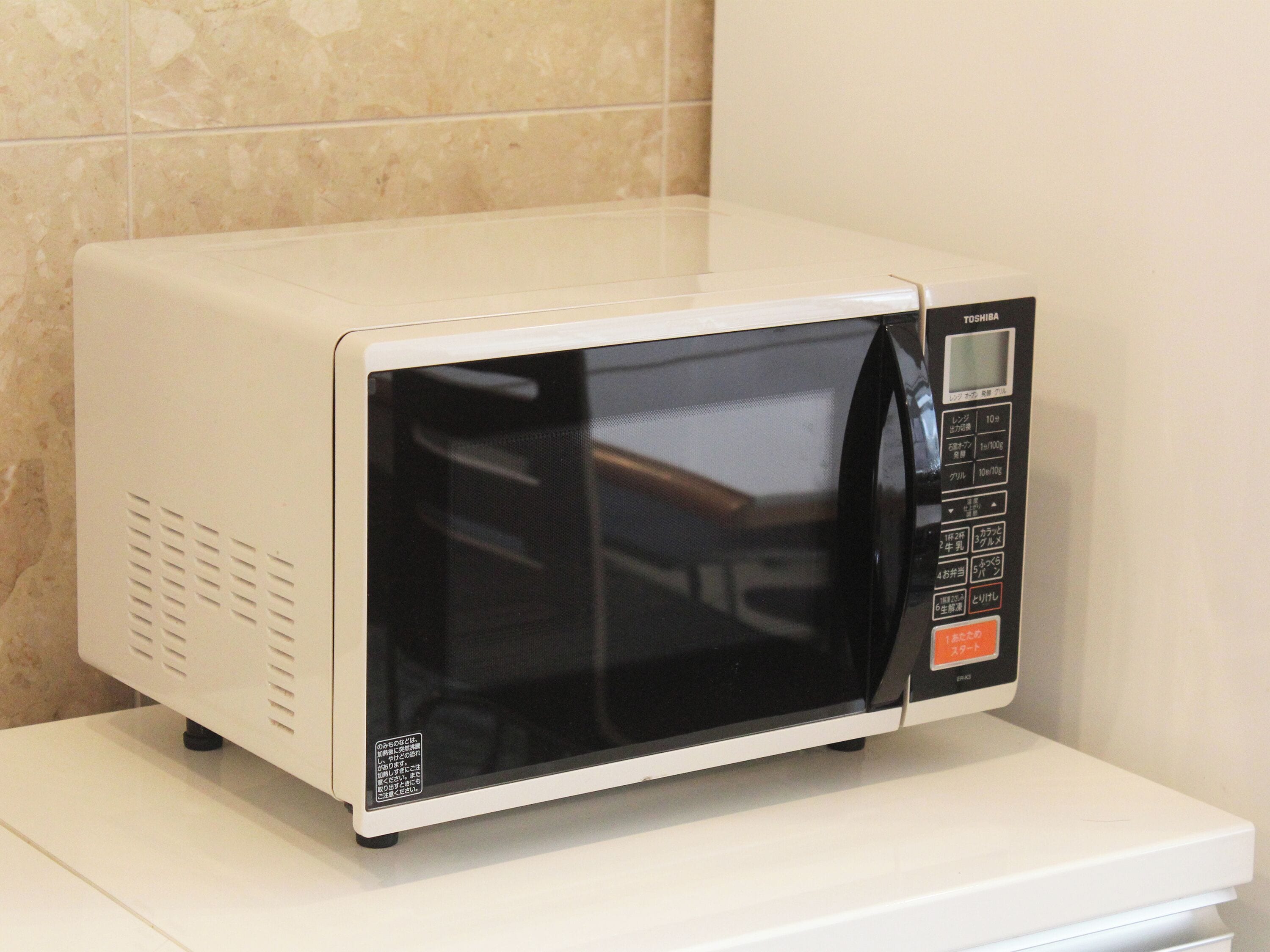Un horno microondas blanco con pantalla digital y panel de control, sobre una encimera blanca.